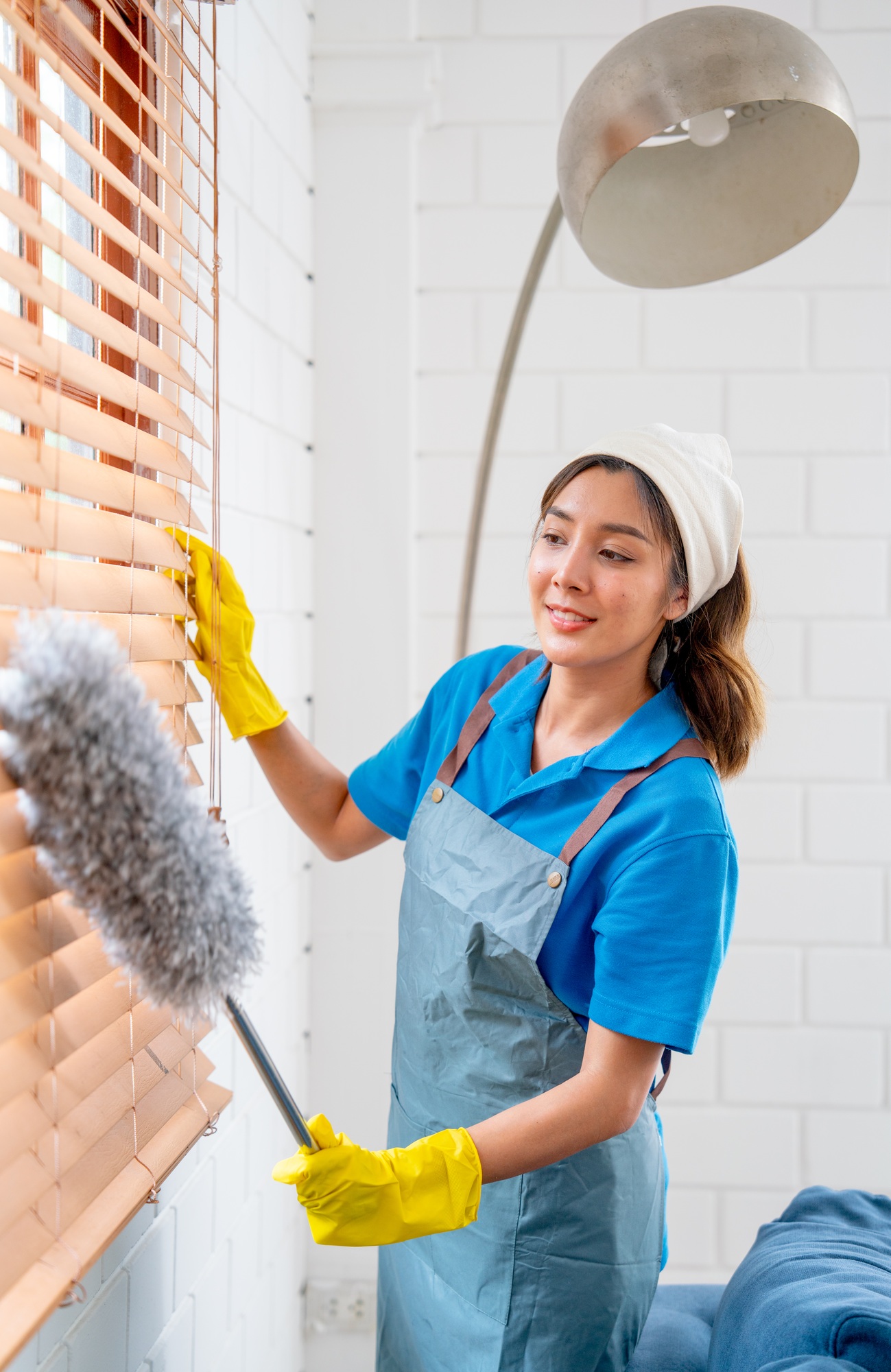 Vertical image of Asian housekeeper or housemaid use feather duster to clean curtain or window shade